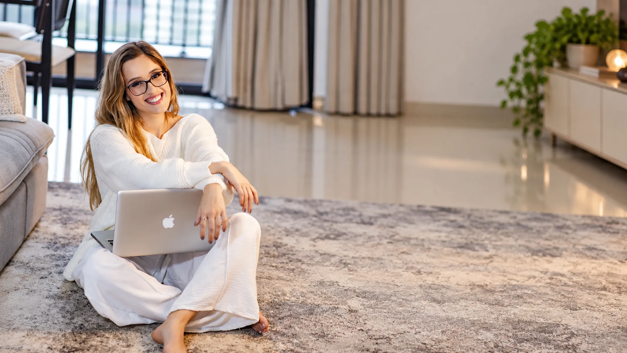 Nathália Garcia sentada no chão da sala com o notebook, sorrindo